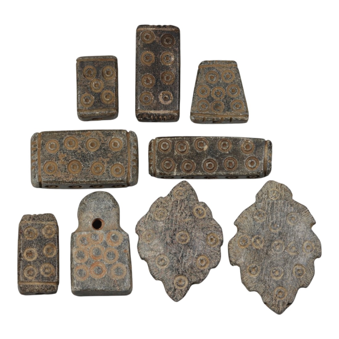 Lot of 9 Ancient Schist Beads with Incised Concentric Circles, Circa Early First Millennium BCE,: Carved from dark grey schist with natural patination, the group consists of nine beads of varying forms, including rectangular, trapezoidal, and leaf-shaped examples. Each piece is decorated with inci