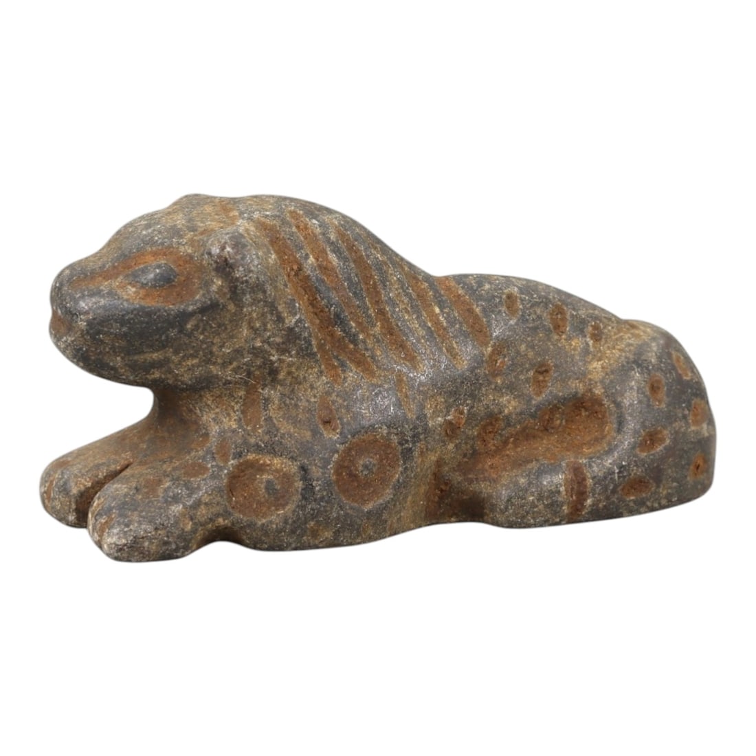 Ancient Stone Zoomorphic Amulet - Near Eastern Feline Figure, 12AM: This amulet is carved from dark stone, depicting a recumbent feline in a crouched posture, with incised linear and circular motifs defining the mane, spots, and facial features. The piece reflects the