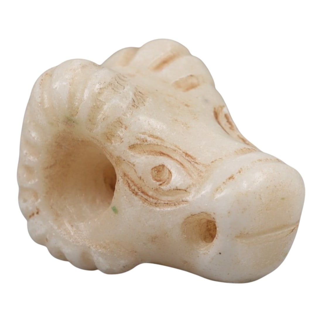 Ancient Marble Ram Head - Near Eastern Amulet Figurine, 17AK: Crafted from pale marble, this miniature amulet depicts a stylized ram's head with prominent, curved horns detailed with incised linear textures. The face features carved eyes, a nasal perforation, an