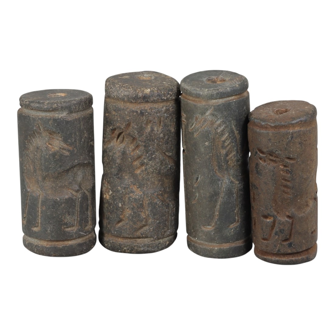 Lot of 4 Ancient Mesopotamian Cylinder Seals, 96WM: A curated lot of four ancient Mesopotamian-style cylinder seals, carved from dark stone with natural patination and wear consistent with age. Each cylindrical seal features a central perforation for u