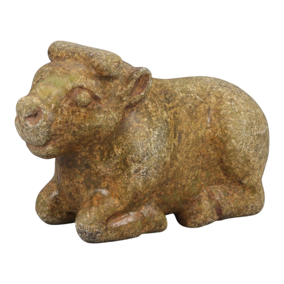 An Achaemenid Serpentine Bovid Figurine, 13YD: Carved from mottled greenish-brown serpentine with areas of surface patination, the figurine depicts a recumbent bovid with the forelegs folded beneath the chest and the hindquarters compactly positio
