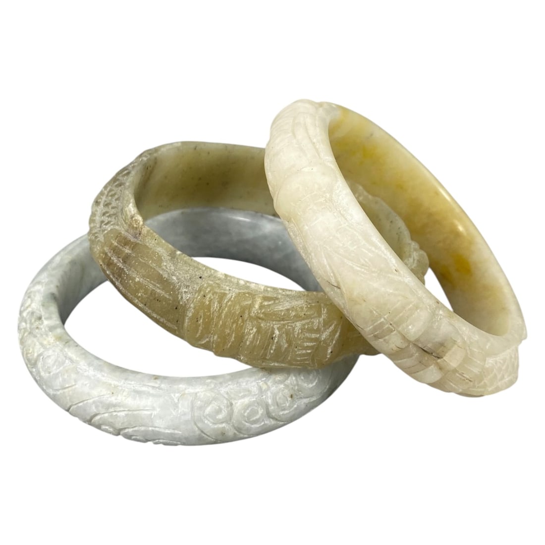 Lot of 3 Chinese Carved Jadeite Jade Bracelets (Bangles), 90AC: Each bracelet is carved from jadeite with varied natural coloration and inclusions, including pale grey-white, mottled greyish-brown, and creamy white with yellowish tones. The outer surfaces feature 