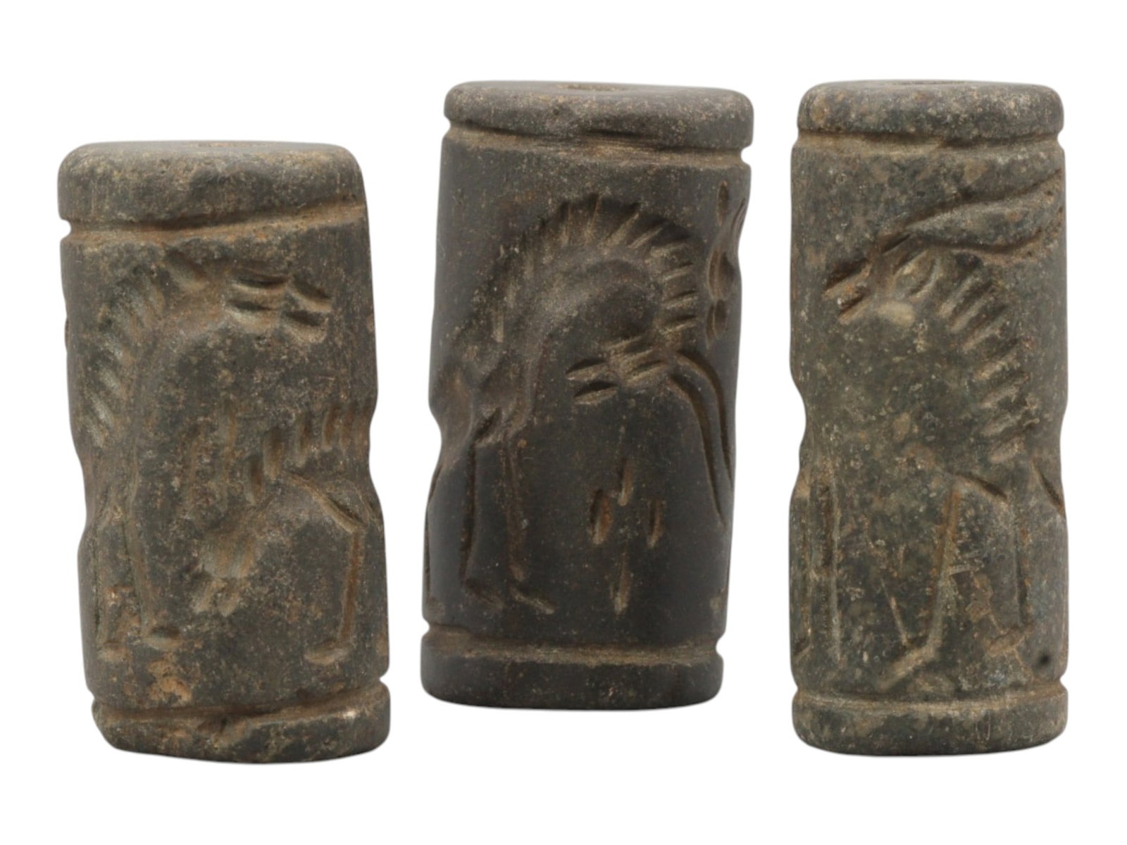 Lot of 3 Ancient Mesopotamian Cylinder Seals, 48WP: A curated lot of three ancient Mesopotamian-style cylinder seals, carved from dark stone with natural patination and wear consistent with age. Each cylindrical seal features a central perforation for 