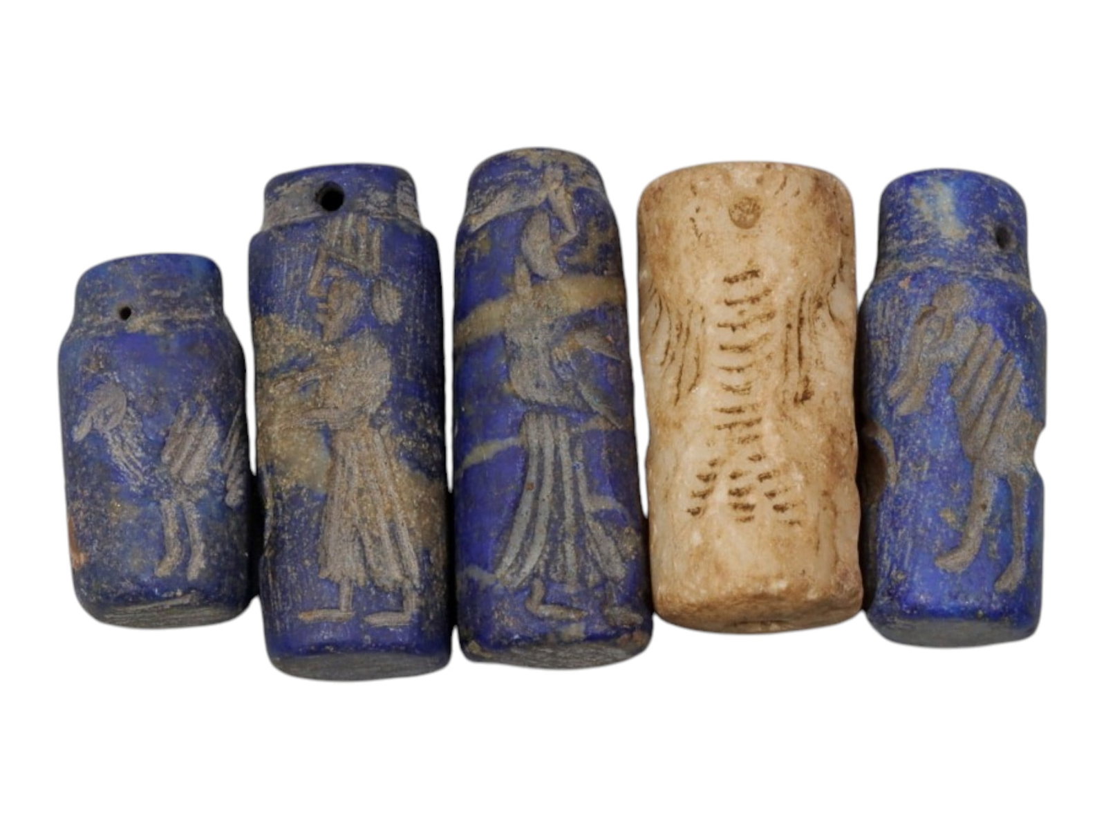 Lot of 5 Ancient Mesopotamian Stone and Lapis Lazuli Cylinder Seals, 75WP: A curated lot of five ancient Mesopotamian-style cylinder seals, including four carved from lapis lazuli and one from light-colored stone, with natural patination and wear consistent with age. Each cy