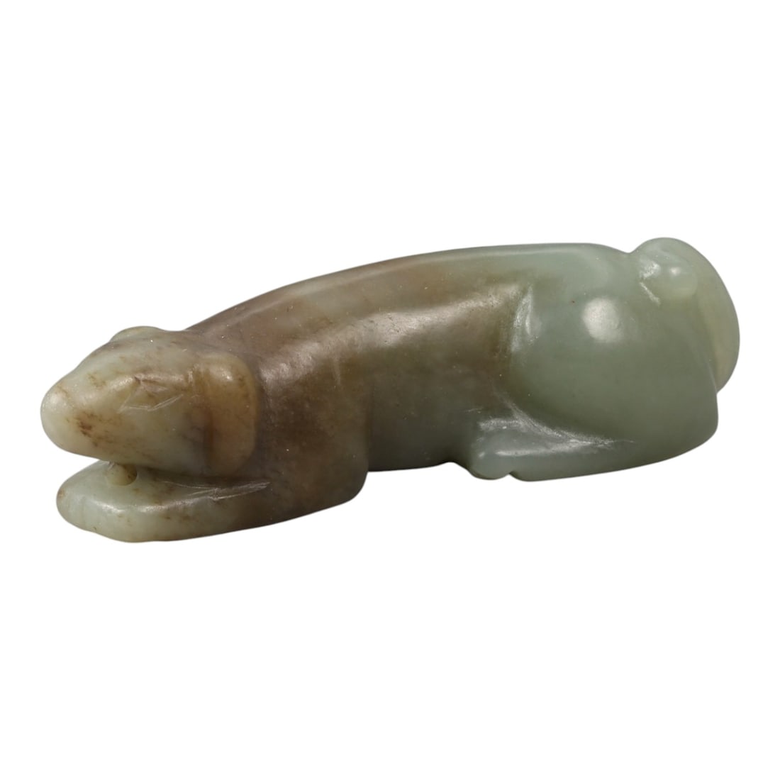 A Chinese Hetian Jade Carved Animal Ornament, 20th Century, 12FD: Carved from pale celadon Hetian jade with areas of warm brown coloration and natural translucency, the object is modeled as a recumbent zoomorphic form shown in profile. The animal is rendered with an