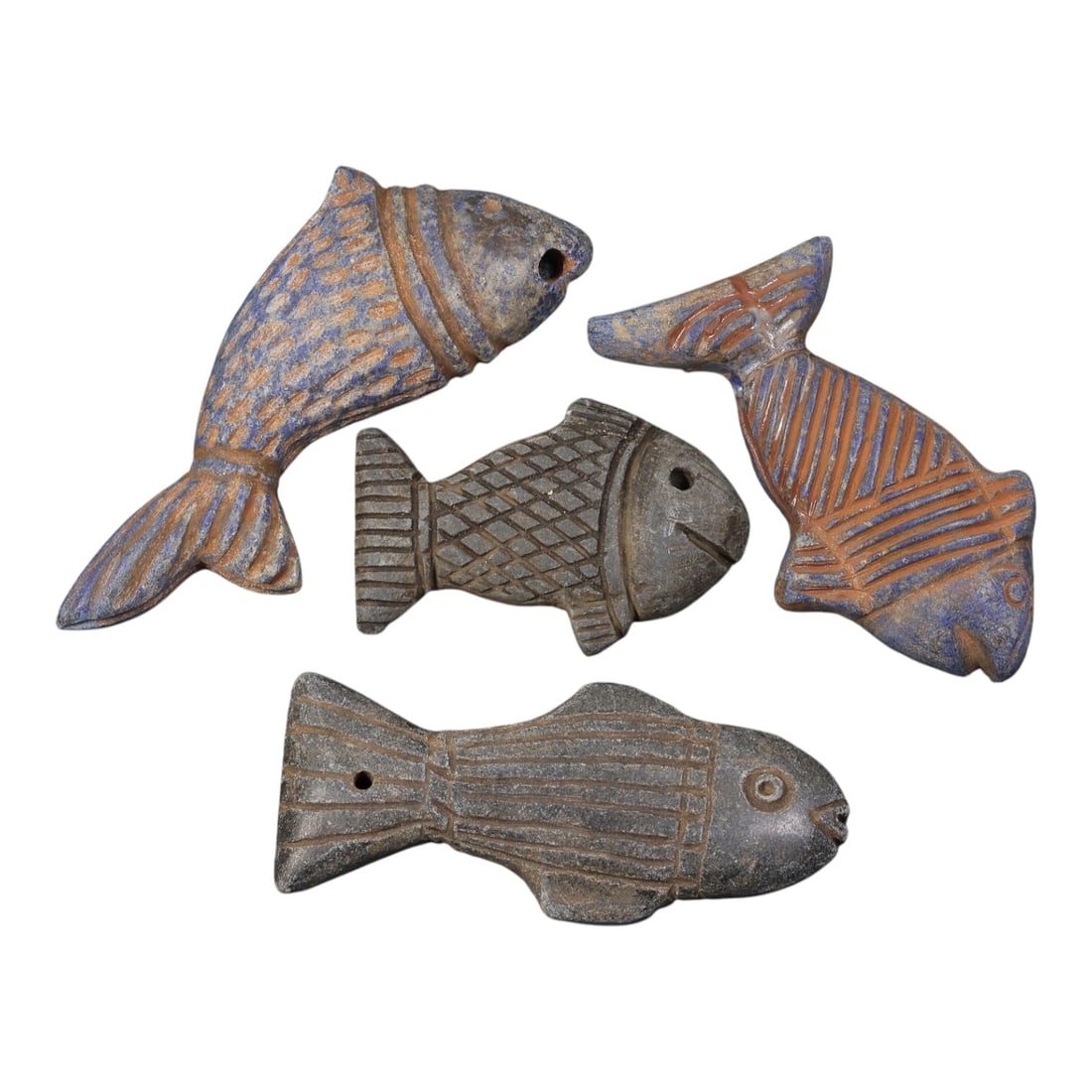 Lot of 4 Ancient Near Eastern Stone Fish Amulets, Circa 1st Millennium BCE, 94AD: Comprising four fish-shaped amulets carved from stone, including lapis lazuli and dark grey stone varieties. Each example features stylized incised decoration representing scales, fins, and tails: one