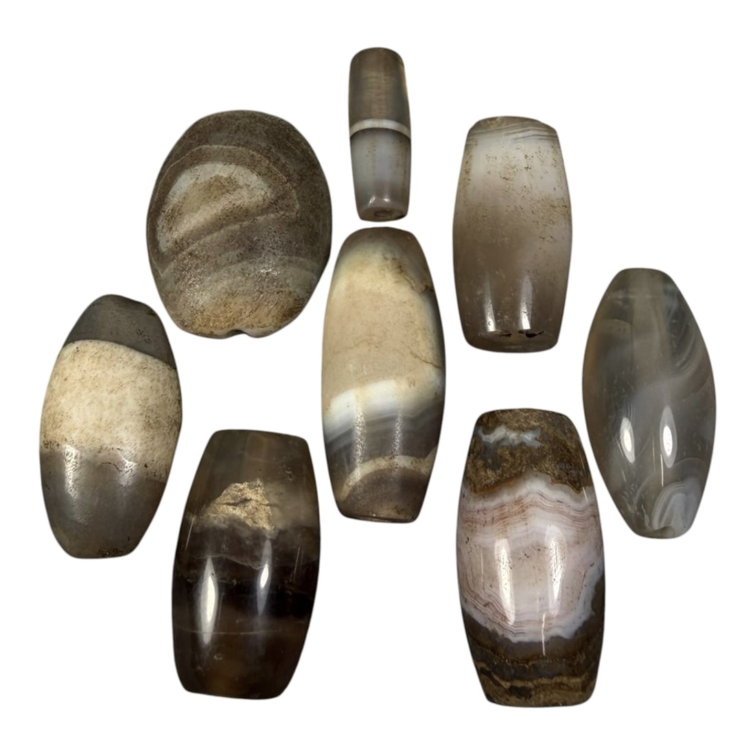 Lot of 8 Himalayan Banded Agate Beads, Ancient to Antique Period, 15AH: A group of eight beads crafted from banded agate, displaying natural variations in tone including translucent grey, brown, cream, and multi-tonal banding patterns. The beads are predominantly barrel-s