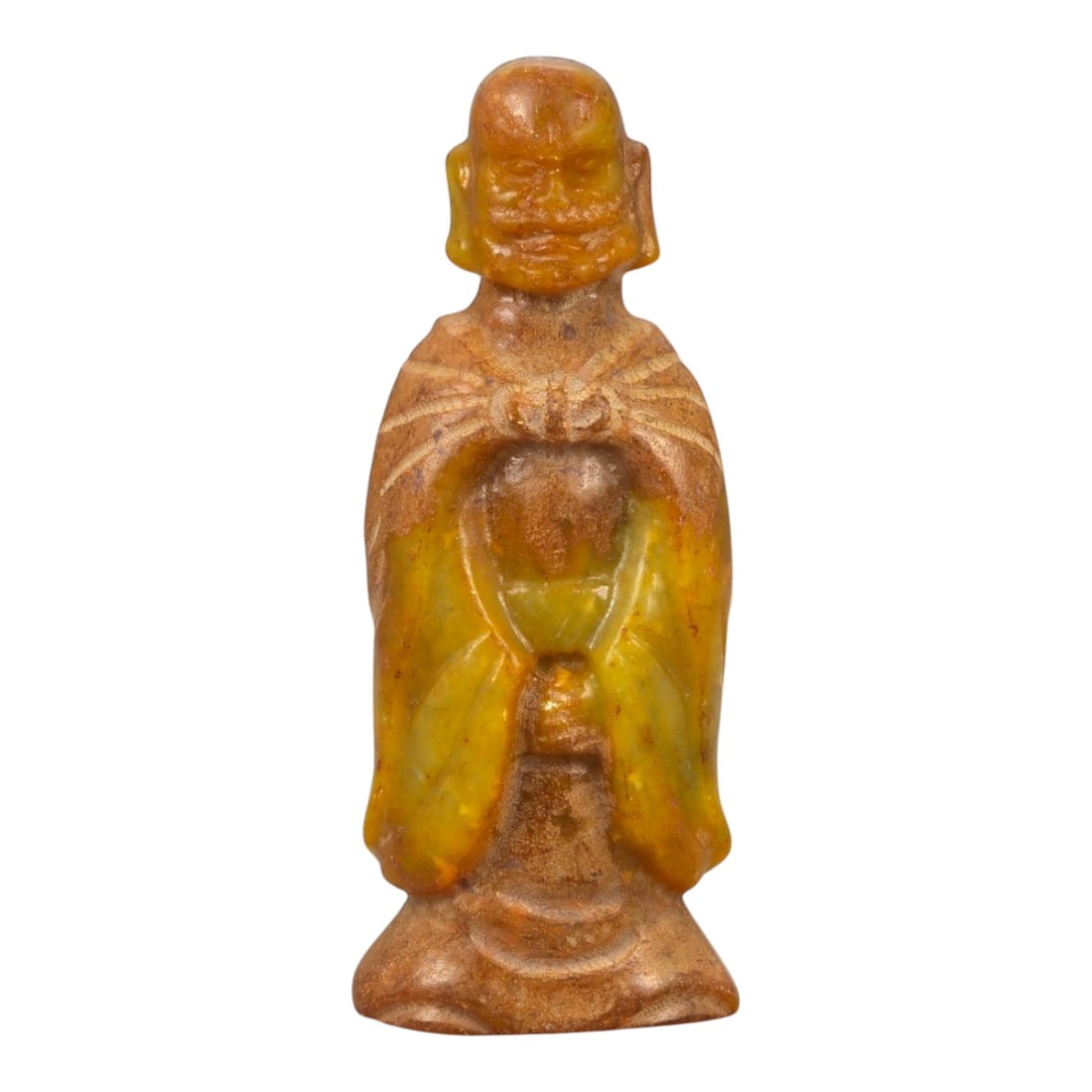 A Chinese Jade Figure of a Standing Monk, 20th Century, 65FB: Carved from translucent yellow to brown-toned jade with areas of darker inclusions and natural surface variation, the figure represents a standing male monk shown frontally. The head is bald, with sim