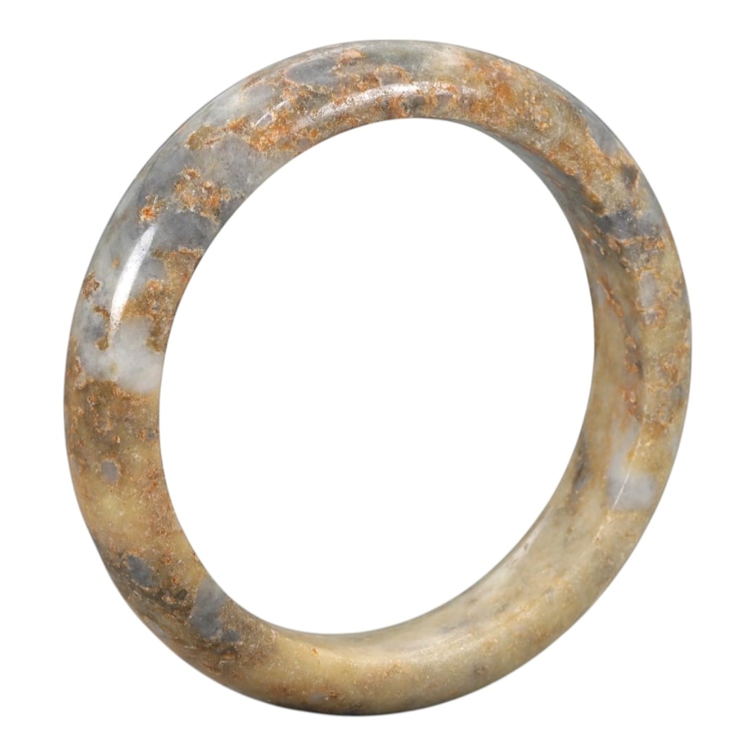 A Chinese Jadeite Jade Bangle Bracelet, 20th Century, 100ZK: Carved from jadeite jade with a pale yellowish-tan base and prominent russet and greyish-blue mineral inclusions concentrated along the upper edge, the bangle is formed as a continuous circular band w