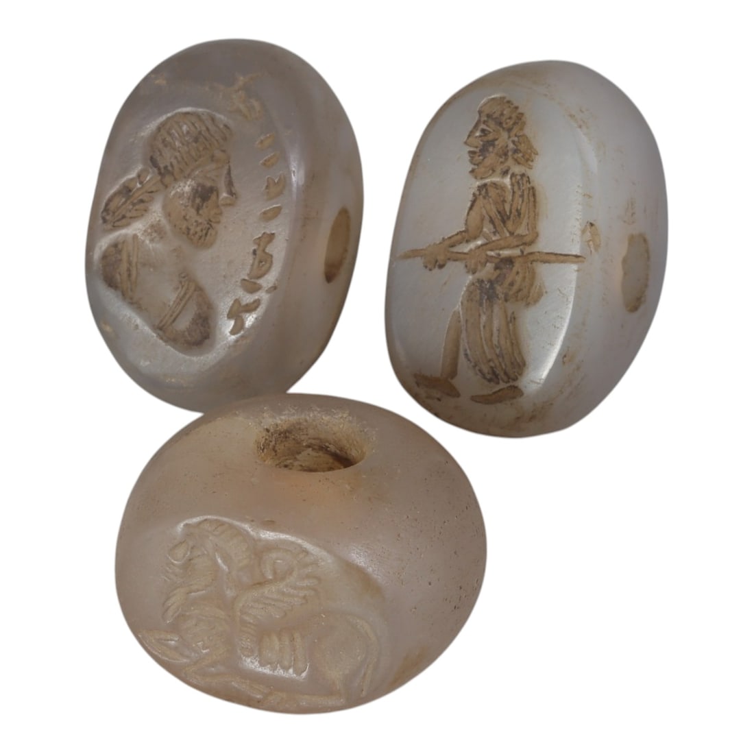 Lot of 3 Ancient Sasanian Chalcedony Stamp Seals, Circa 3rd-7th Century CE, 55WP: A collection of three Sasanian period stamp seals, expertly carved from translucent chalcedony stone, each featuring a central drilled hole for suspension. The seals display characteristic Sasanian ic