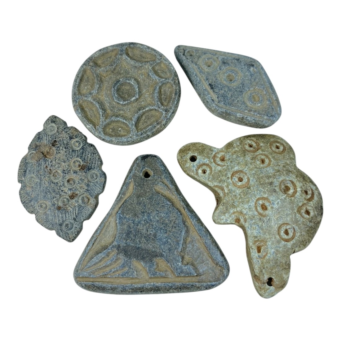 A Lot of 5 Ancient Schist Stone Relics, 93AB: The group comprises five ancient schist stone artifacts of varied forms, including circular, leaf-shaped, triangular, and stylized animal forms, all exhibiting weathered grey and light beige tones wit