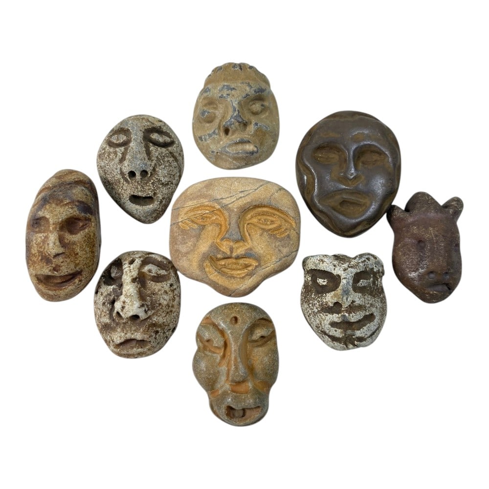 A Lot of 9 Ancient Medieval Stone Maskette Amulets, 3AB: The group comprises nine carved stone maskette amulets, each depicting stylized human faces, with one example featuring zoomorphic attributes. The faces are rendered in varied styles, some with deeply