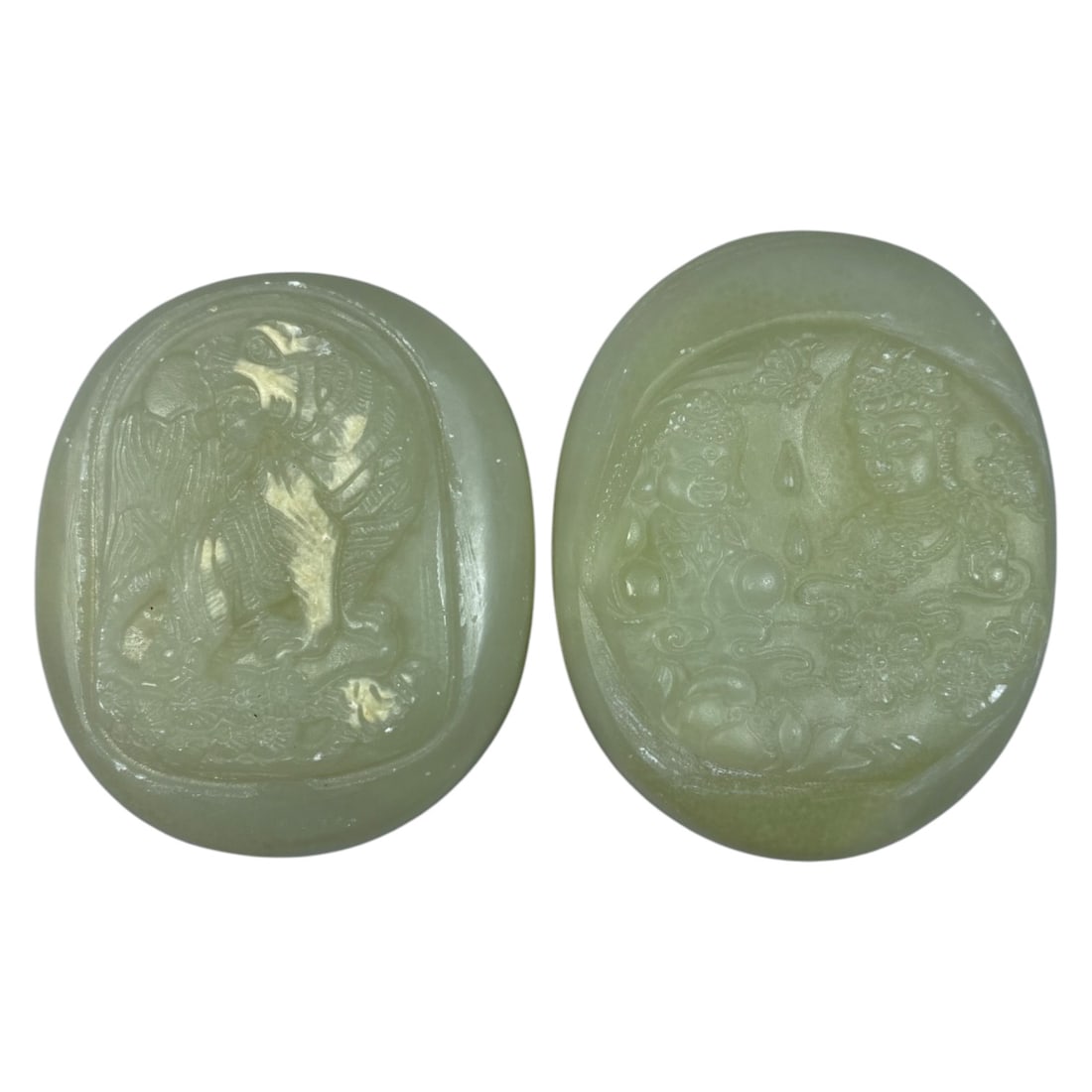 Lot of 2 Vintage Oriental Chinese Nephrite Jade Plaques, 58AG: The lot comprises two oval nephrite jade plaques, both carved from pale celadon stone with a smooth, polished finish. The left plaque features a relief carving of a mythical guardian lion (foo dog) am