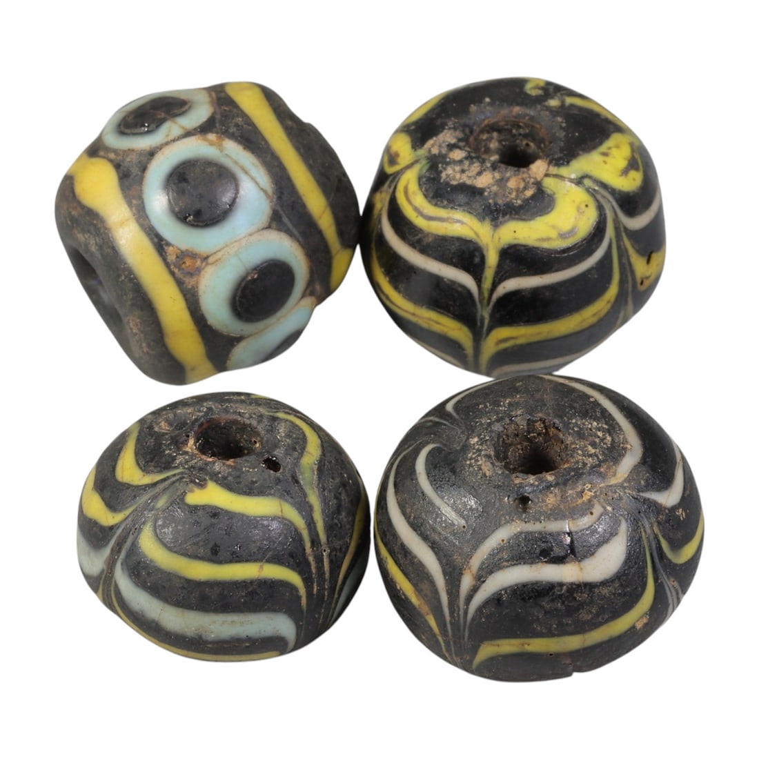 Lot of 4 Antique Islamic Feather & Eye-Patterned Glass Beads, Circa 9th-14th Century, 41WM: A group of four glass beads, varying in form from spherical to barrel-shaped, all with central perforations. The beads display two distinct decorative styles: feather-patterned trailed glass in contra