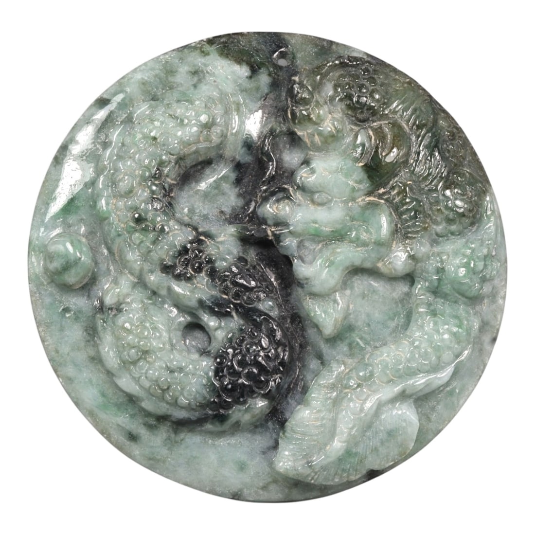 A Chinese Jade Carved Roundel, 20th Century, 4ZB: Carved from mottled green and dark-toned jade, the roundel is worked in high relief with a sinuous dragon shown in profile encircling a central aperture. The surface displays graduated scaling, a ridg