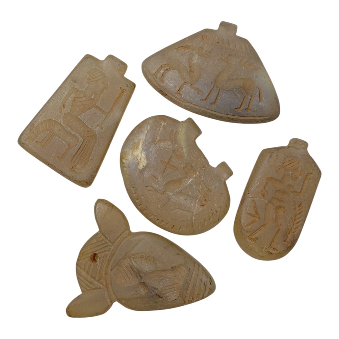 A Lot of 5 Ancient Chalcedony Amulet Pendants, 14AC: The group comprises five amulet pendants carved from pale, translucent chalcedony, exhibiting natural color variations, surface patina, and signs of age consistent with antiquity. Each pendant feature