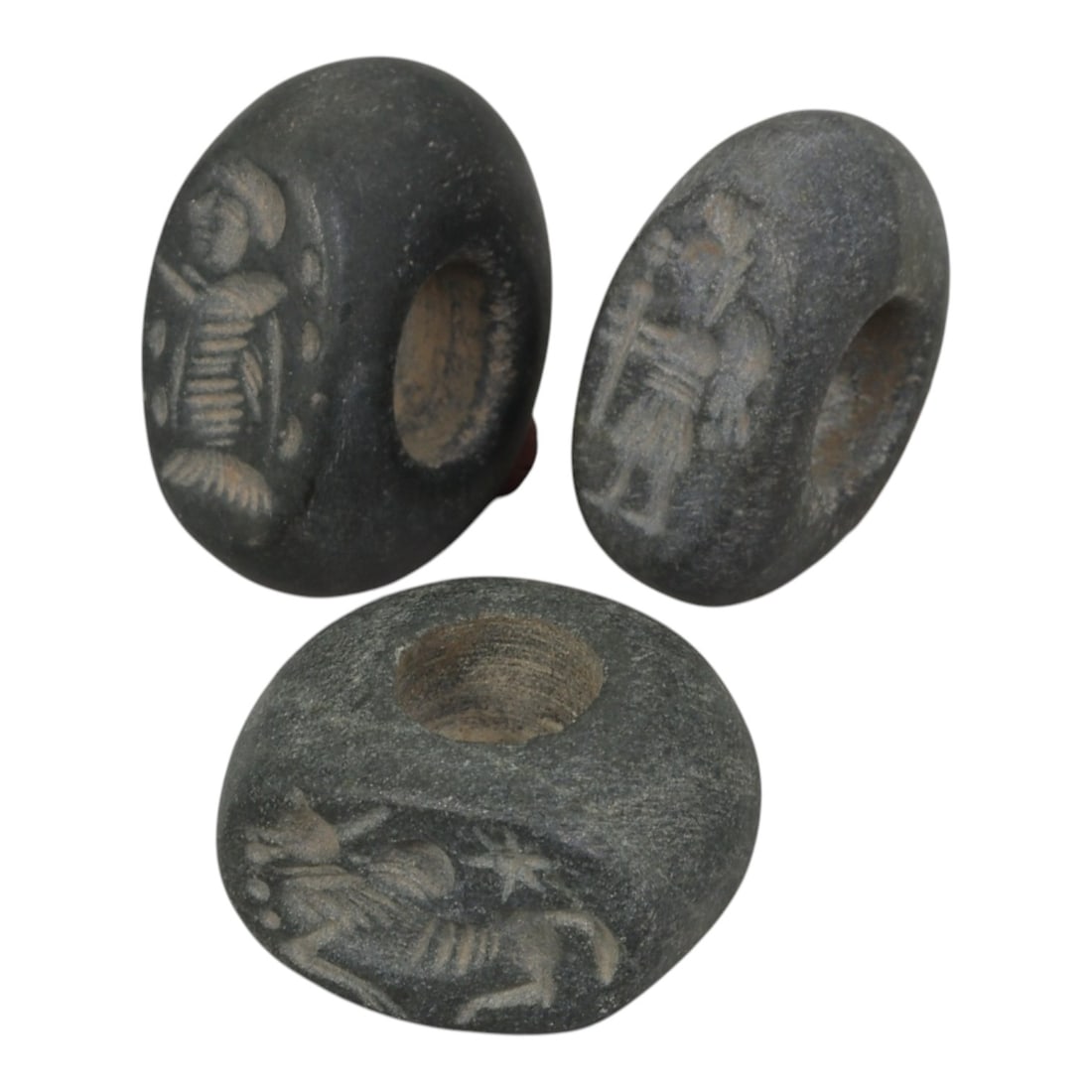 Lot of 3 Sasanian Stone Stamp Seals, Circa 3rd-7th Century CE, 66WM: A group of three Sasanian period stamp seals carved from dark grey stone, each featuring a central perforation for suspension. The seals are incised with distinct motifs typical of Sasanian glyptic ar