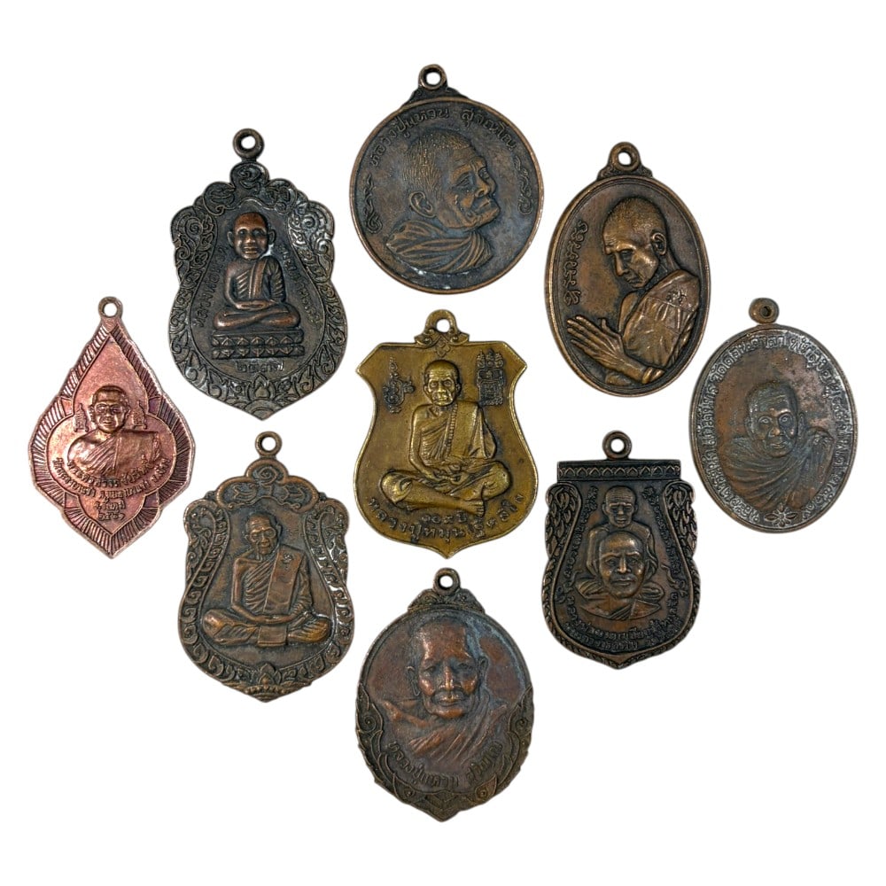 A Lot of 9 Vintage Thai Copper and Bronze Monk Amulets, 46AA: Comprising 9 unmounted pendants ranging from 3.5 to 4.5 cm in height. The collection features a variety of cast metal amulets depicting revered Thai Buddhist monks, including bust portraits and seated
