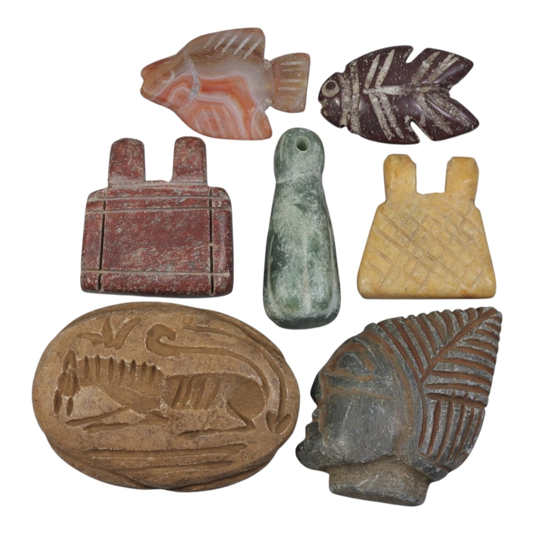 Lot of 7 Ancient Coptic Egyptian Multi-Stone Amulets, Circa Roman to Coptic Era, 92AH: Carved from diverse materials including banded carnelian, reddish-brown stone, green serpentine, yellow marble, light brown stone, and dark grey stone, the group consists of seven distinct amulets, ra