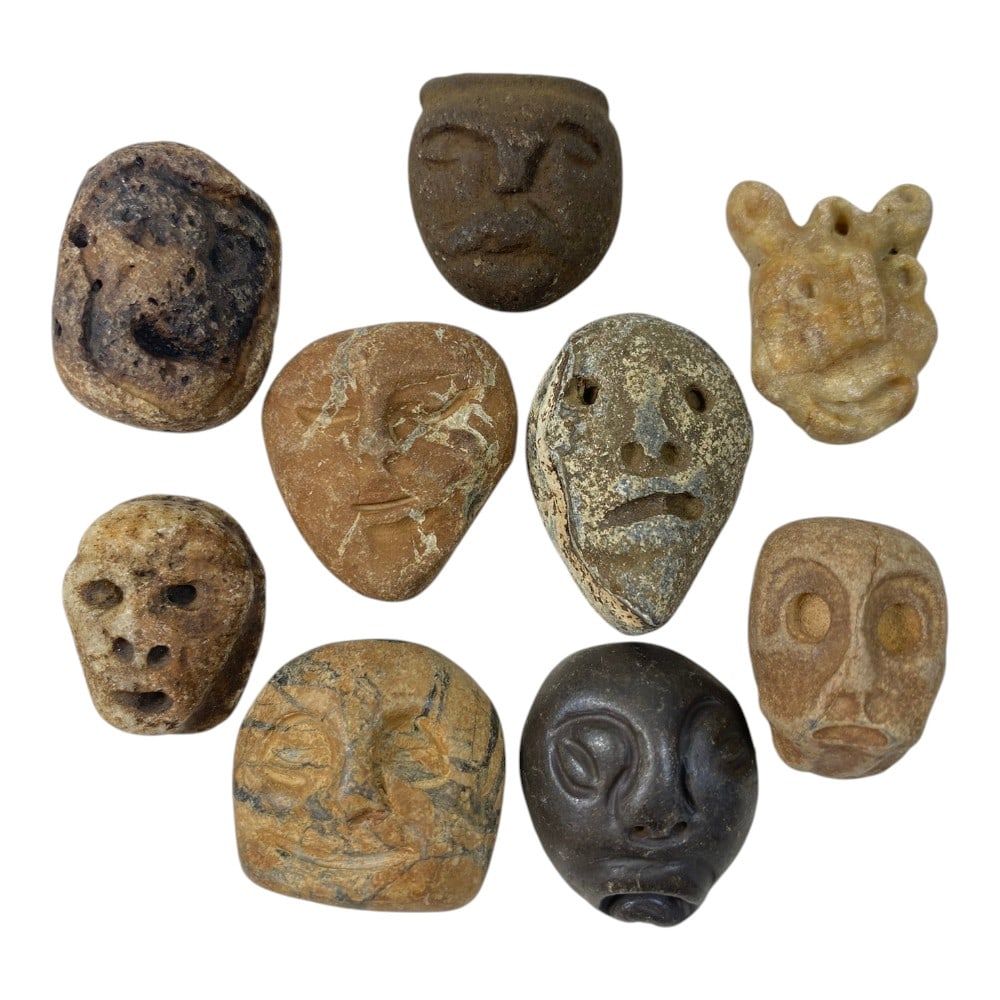 A Lot of 9 Ancient Medieval Stone Maskette Amulets, 5AB: The group comprises nine carved stone maskette amulets, depicting stylized human and zoomorphic faces. The pieces vary in detail, with examples ranging from deeply defined facial features to more sche