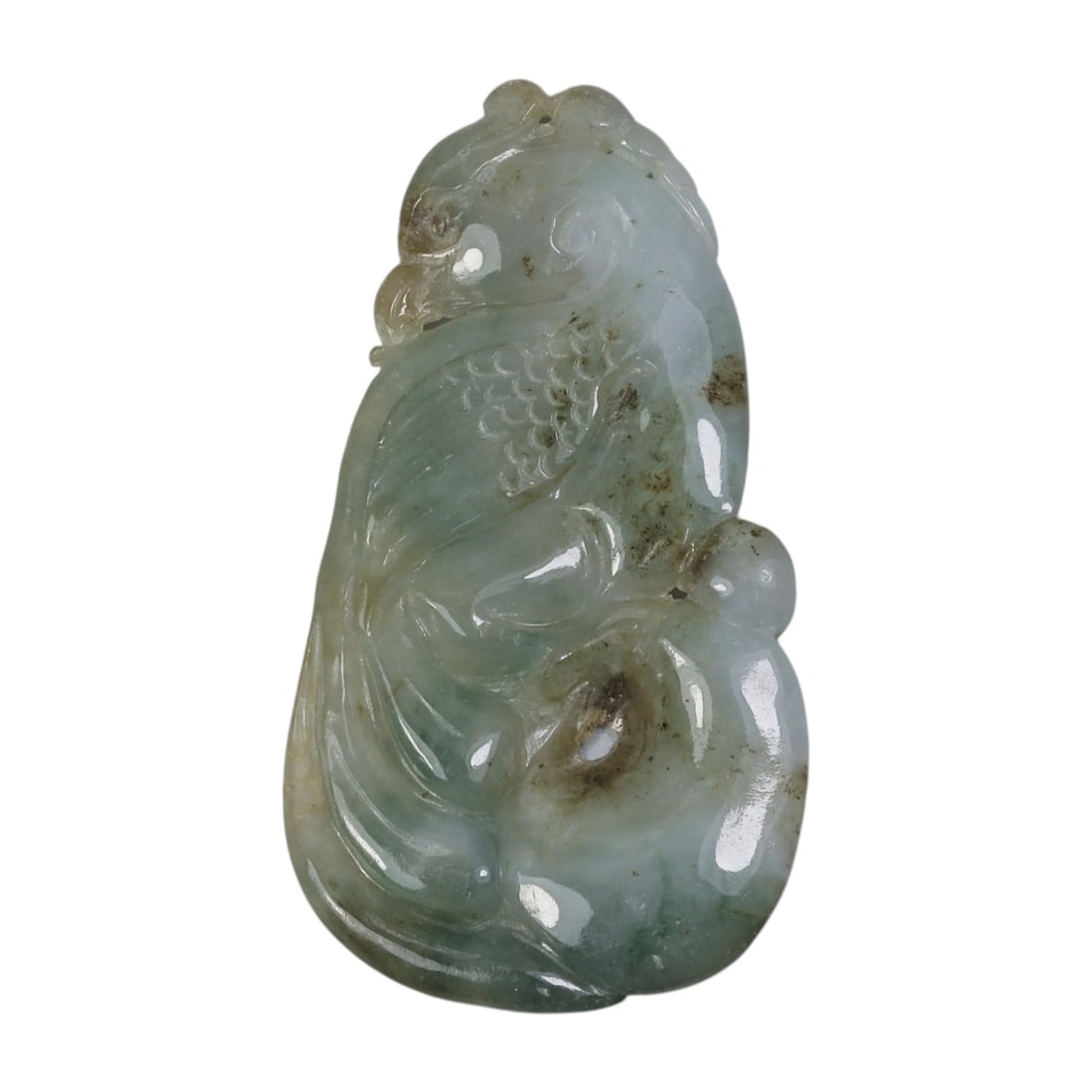 An Antique Oriental Chinese Jadeite Jade Bird Pendant, 40AG: Carved from pale green and white jadeite jade with natural brownish inclusions and subtle tonal variations, the pendant depicts a stylized bird form. The bird is shown in profile with incised feather 