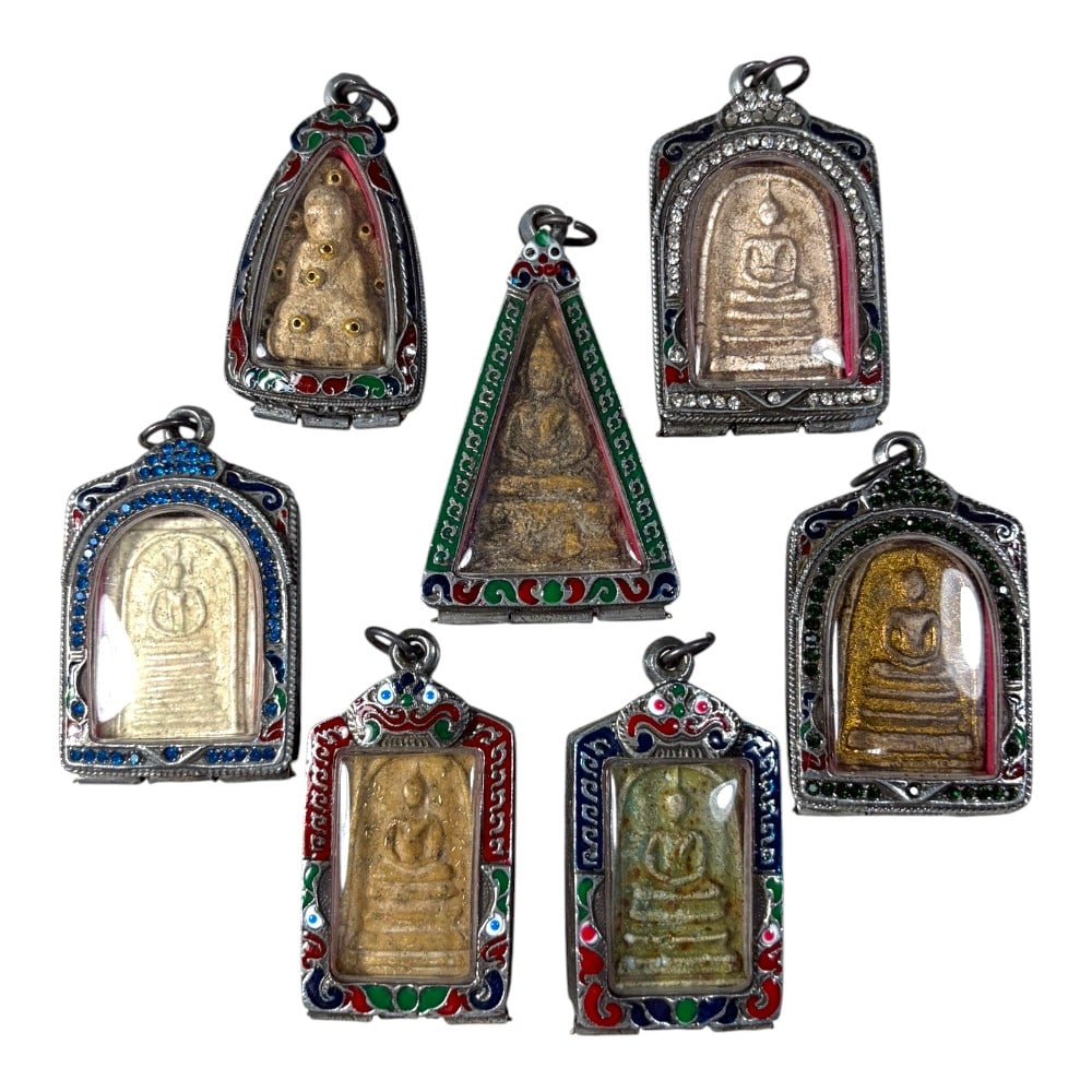 A Lot of 7 Vintage Thai Buddhist Amulets with Enamel and Jewel Accented Cases, 41AA: Comprising seven pendants ranging from 6 to 7 cm in height. Each amulet features an aged seated Buddha image, encased in ornate silver-toned metal cases. The cases are richly decorated with vibrant en