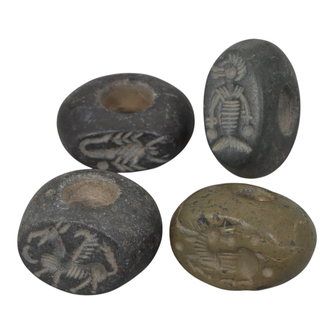 Lot of 4 Ancient Sasanian Stone Stamp Seals, Circa 3rd-7th Century CE, 74WP: A collection of four Sasanian period stamp seals, carved from various dark and greenish stone types, each with a central drilled hole for suspension. The seals are decorated with characteristic Sasani