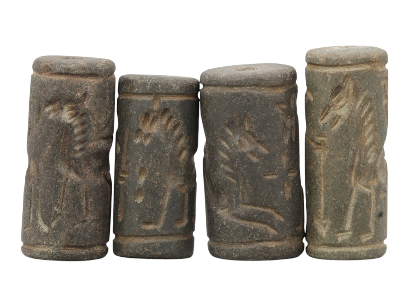 Lot of 4 Ancient Mesopotamian Cylinder Seals, 50WP: A curated lot of four ancient Mesopotamian-style cylinder seals, carved from dark stone with natural patination and wear consistent with age. Each cylindrical seal features a central perforation for u