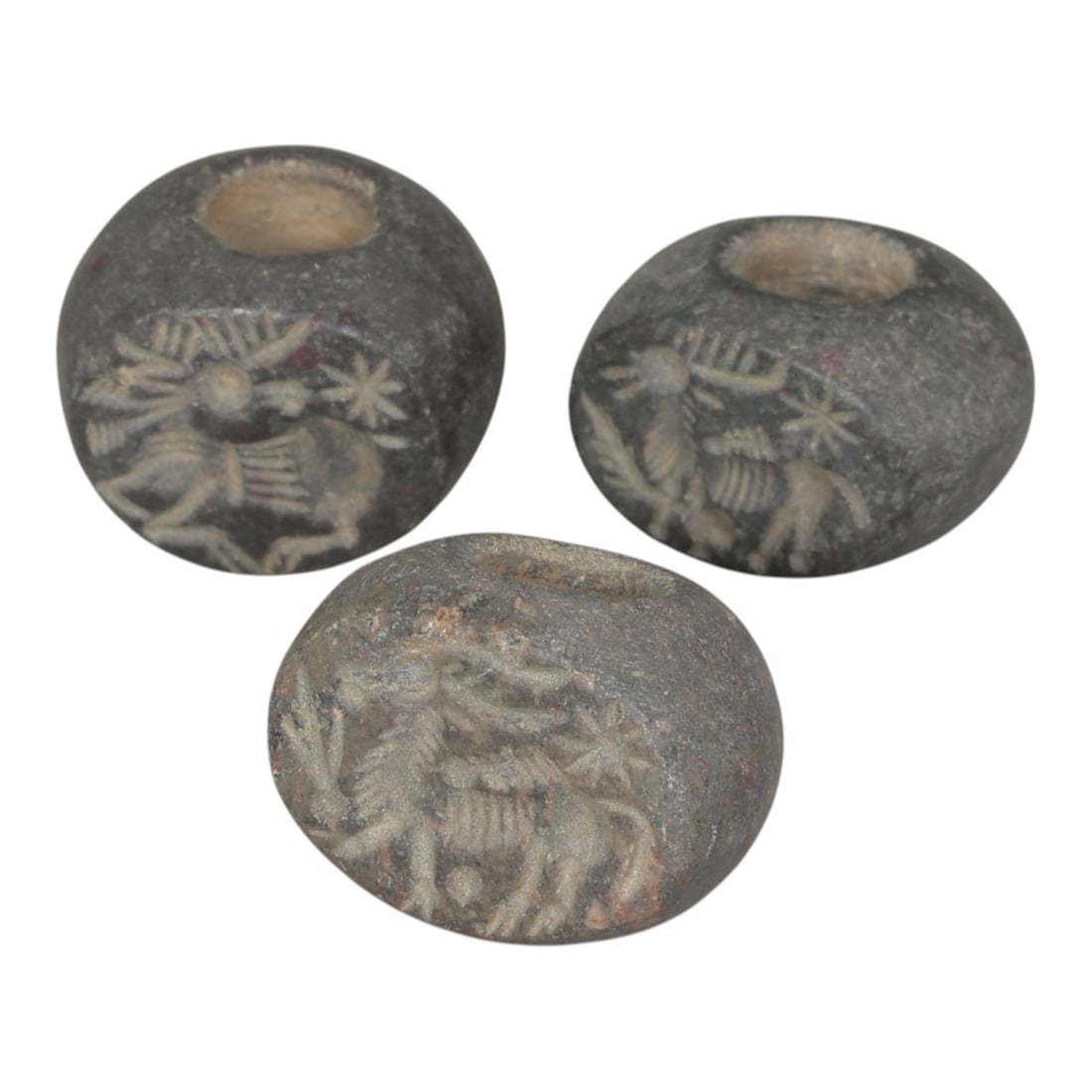 Lot of 3 Sasanian Stone Stamp Seals, Circa 3rd-7th Century CE, 12AG: Comprising three seals carved from dark grey stone with natural patina and surface wear consistent with ancient use. Each seal is of flattened disc form with a central perforation for suspension. The 