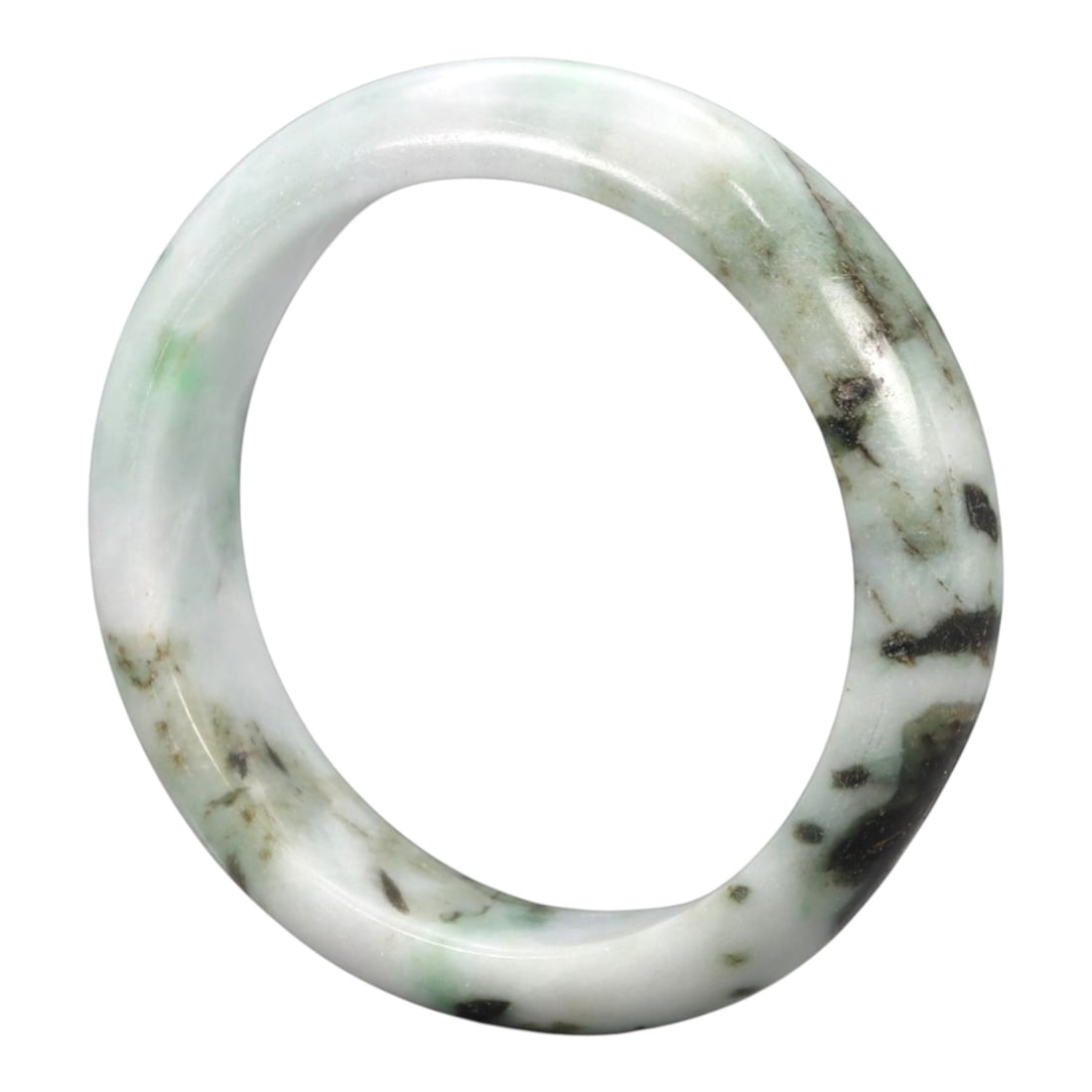 A Chinese Jadeite Jade Bangle Bracelet, 20th Century, 88ZK: Carved from jadeite jade with a pale white base and scattered dark green and black inclusions, the bangle is formed as a continuous circular band with a rounded cross-section. The surface is smoothly 