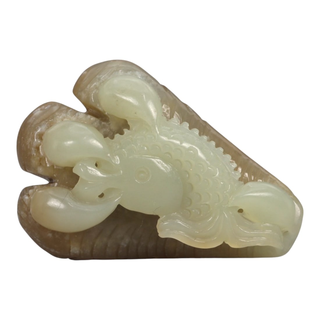 A Chinese Jade Claw with Fish Carving, 20th Century, 1FB: Carved from bi-colored jade with a creamy pale green body contrasted by a warm brown outer skin, the object is worked in the round as a stylized claw grasping a fish. The claw is rendered with three c