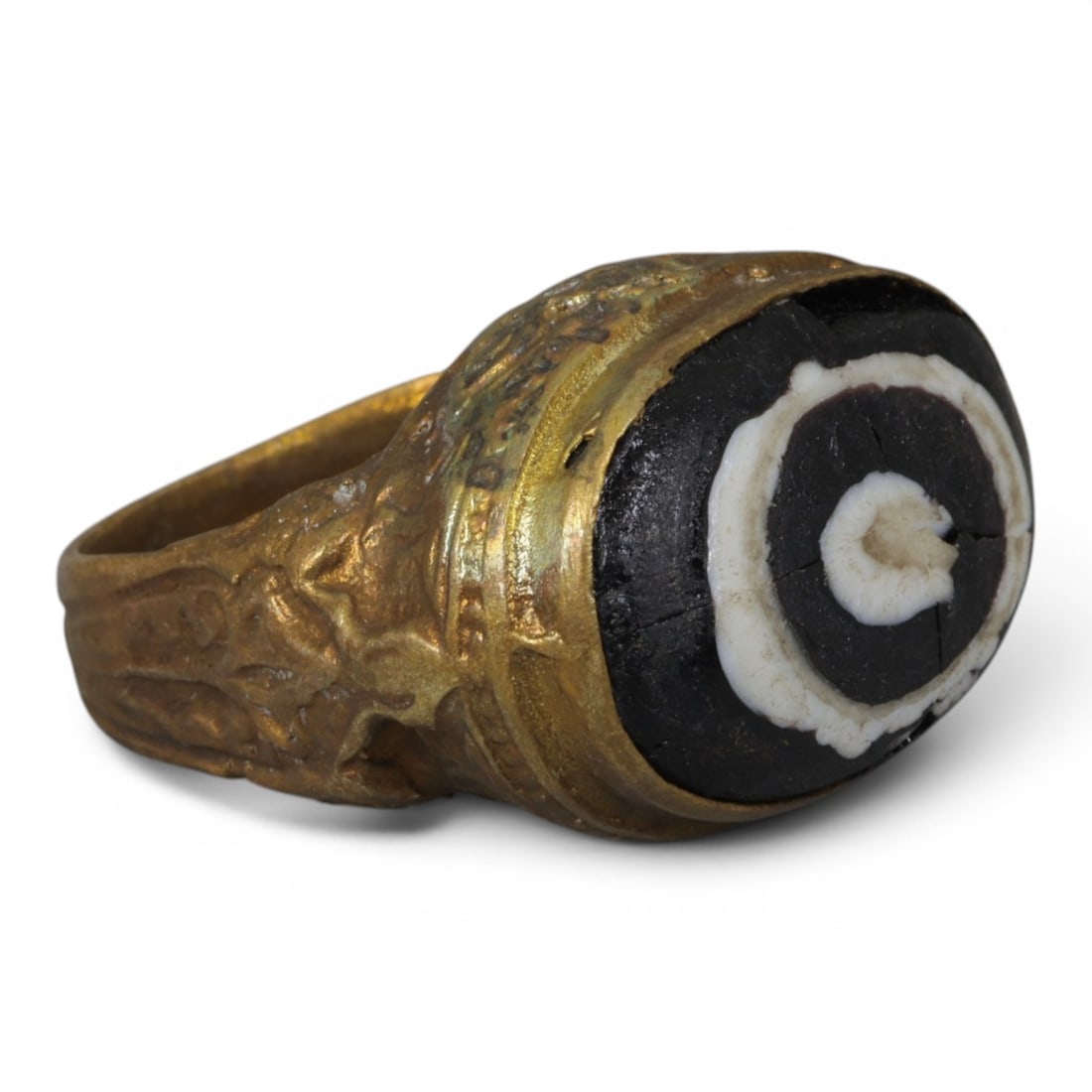 Antique Qajar Dynasty Gilt Evil Eye Ring, US Size 7.5, 17AJ: A gilt-metal ring of the Qajar period, US ring size 7.5, featuring an oval evil-eye glass inlay with a bold concentric black-and-white design (the glass exhibits age-related cracks). The bezel and wid