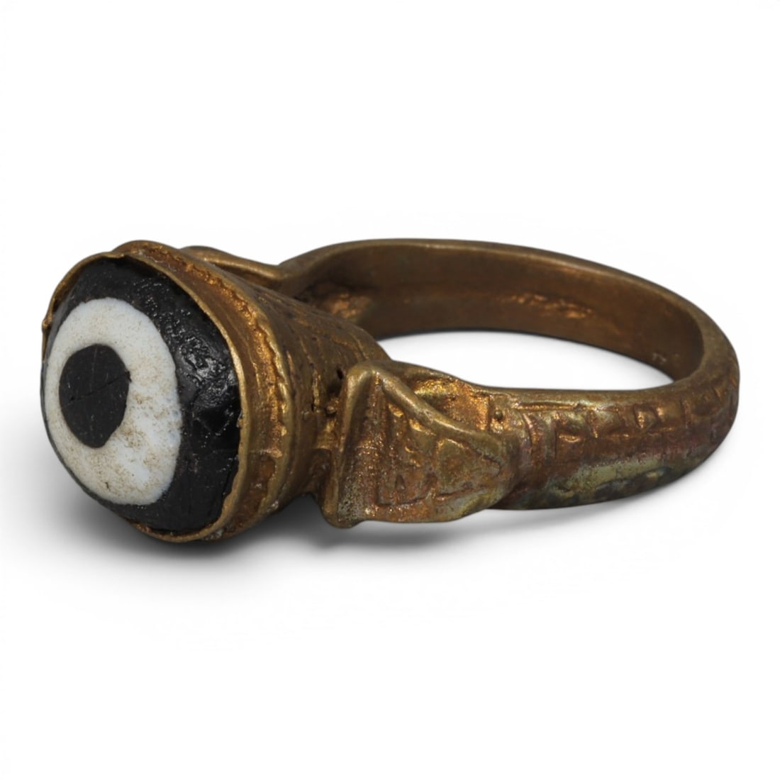 Antique Qajar Dynasty Gilt Evil Eye Ring, US Size 9, 13AJ: A gilt-metal ring of the Qajar period, US ring size 9, featuring a domed evil-eye glass inlay with a bold concentric black-and-white design (the glass exhibits age-related cracks). The bezel is adorne