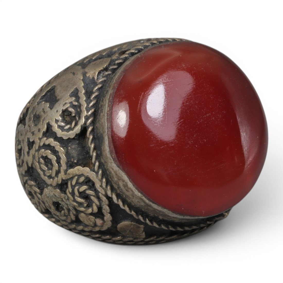 Antique Central Asian Silver and Carnelian Tribal Ring, 19th-Early 20th Century, 33AJ: The ring is set with a large, smooth cabochon carnelian stone. The silver mount is decorated with pseudo-filigree wirework and applied coiled motifs, set against a darkened background. The metal exhib