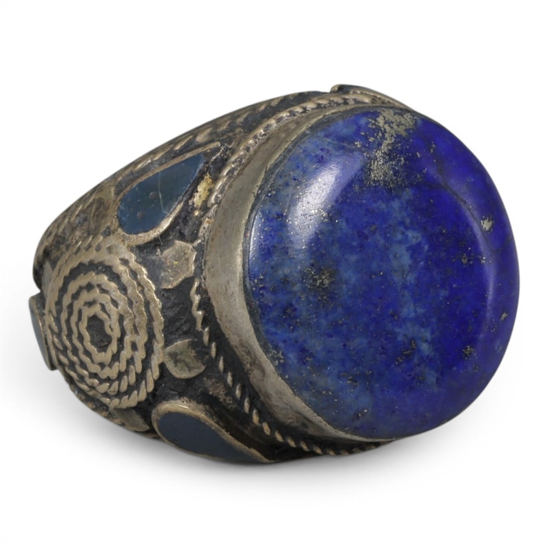 Antique Central Asian Silver and Lapis Lazuli Tribal Ring, 19th-Early 20th Century, 64AJ: The ring is set with a large, smooth cabochon lapis lazuli stone, displaying characteristic pyrite inclusions within its deep blue matrix. The silver mount is decorated with pseudo-filigree wirework, 