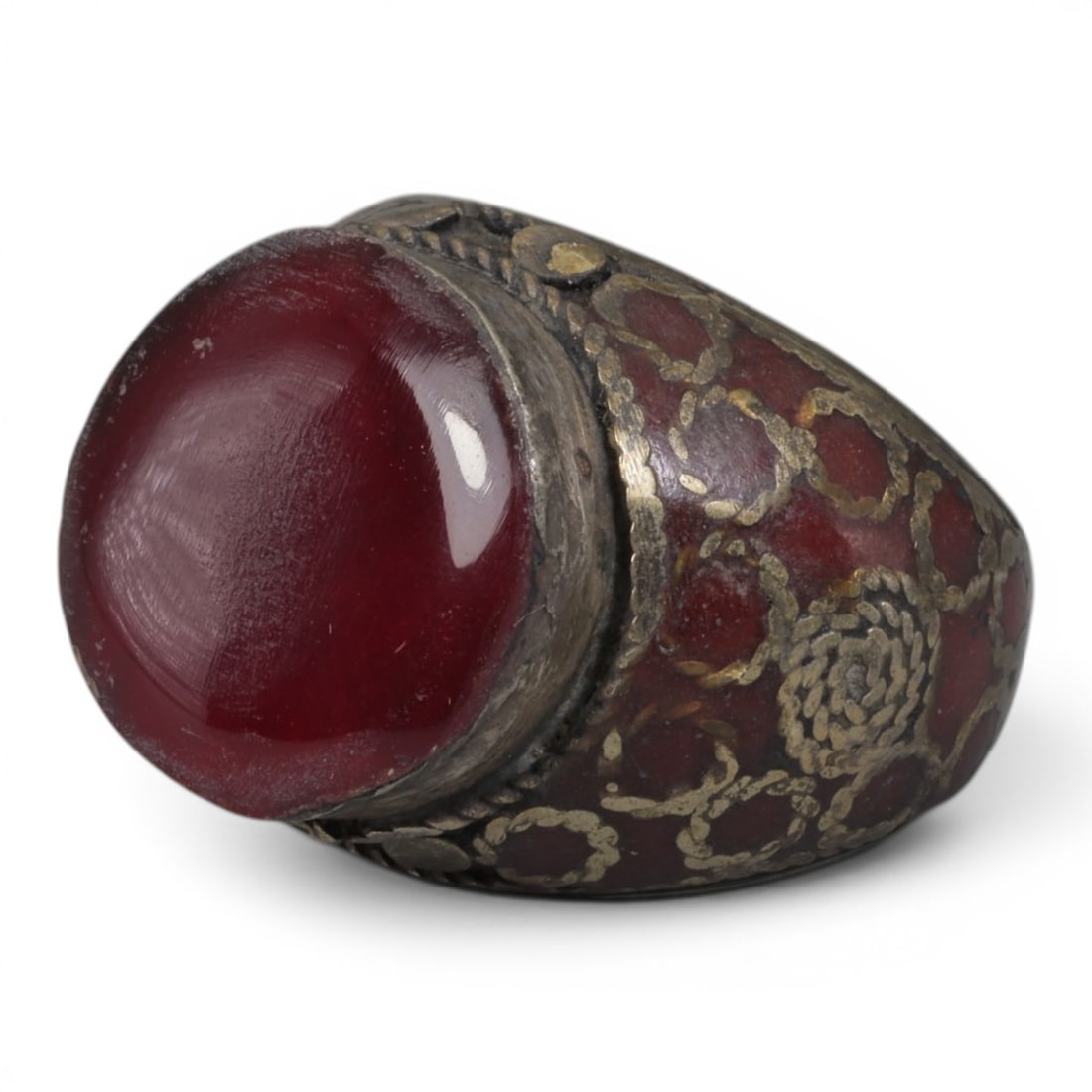 Antique Central Asian Silver and Carnelian Tribal Ring, 19th-Early 20th Century, 57AJ: The ring is set with a large, smooth cabochon carnelian stone. The silver mount is decorated with pseudo-filigree wirework over a red-enameled background, featuring applied coiled and circular motifs.
