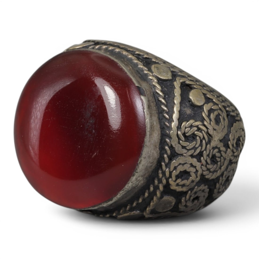 Antique Central Asian Silver and Carnelian Tribal Ring, 19th-Early 20th Century, 58AJ: The ring is set with a large, smooth cabochon carnelian stone. The silver mount is decorated with pseudo-filigree wirework and applied coiled motifs, set against a darkened background. The metal exhib