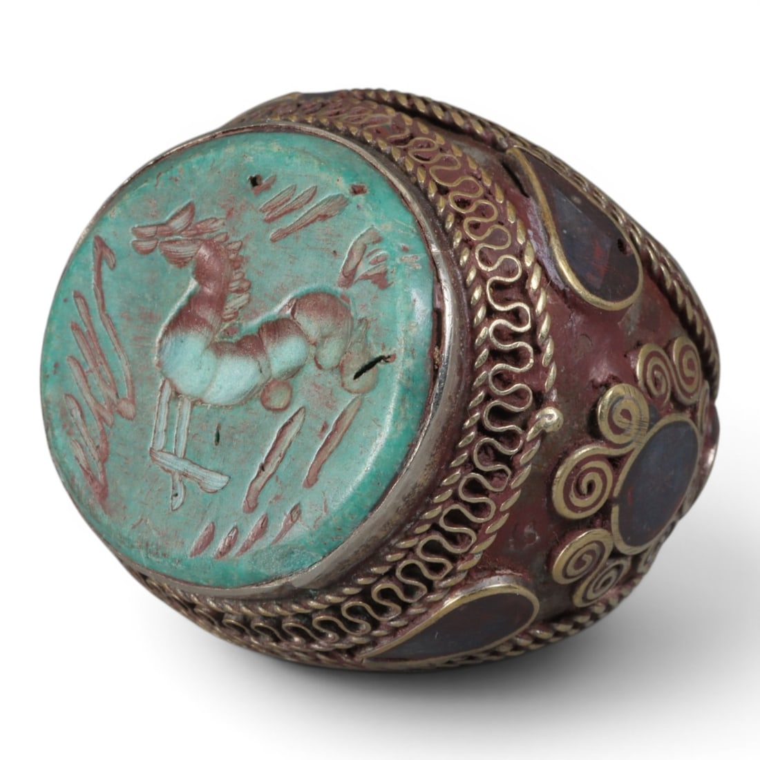 Antique Central Asian Silver and Turquoise Intaglio Tribal Ring, 19th-Early 20th Century: The ring is set with a circular turquoise plaque carved with an intaglio depicting a stylized quadruped, possibly a horse, in profile, with red pigment filling the incised details. The silver mount is
