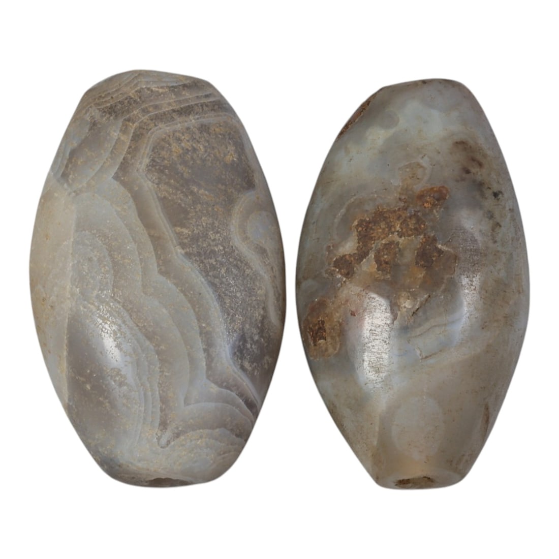 A Pair of Antique Central Asian / Himalayan Banded Agate Trade Beads, 15th-19th Century, 70AK: The pair consists of two large, ovoid banded agate beads. The left bead features distinct, layered grey and white banding with visible surface patina, while the right bead displays a more translucent 