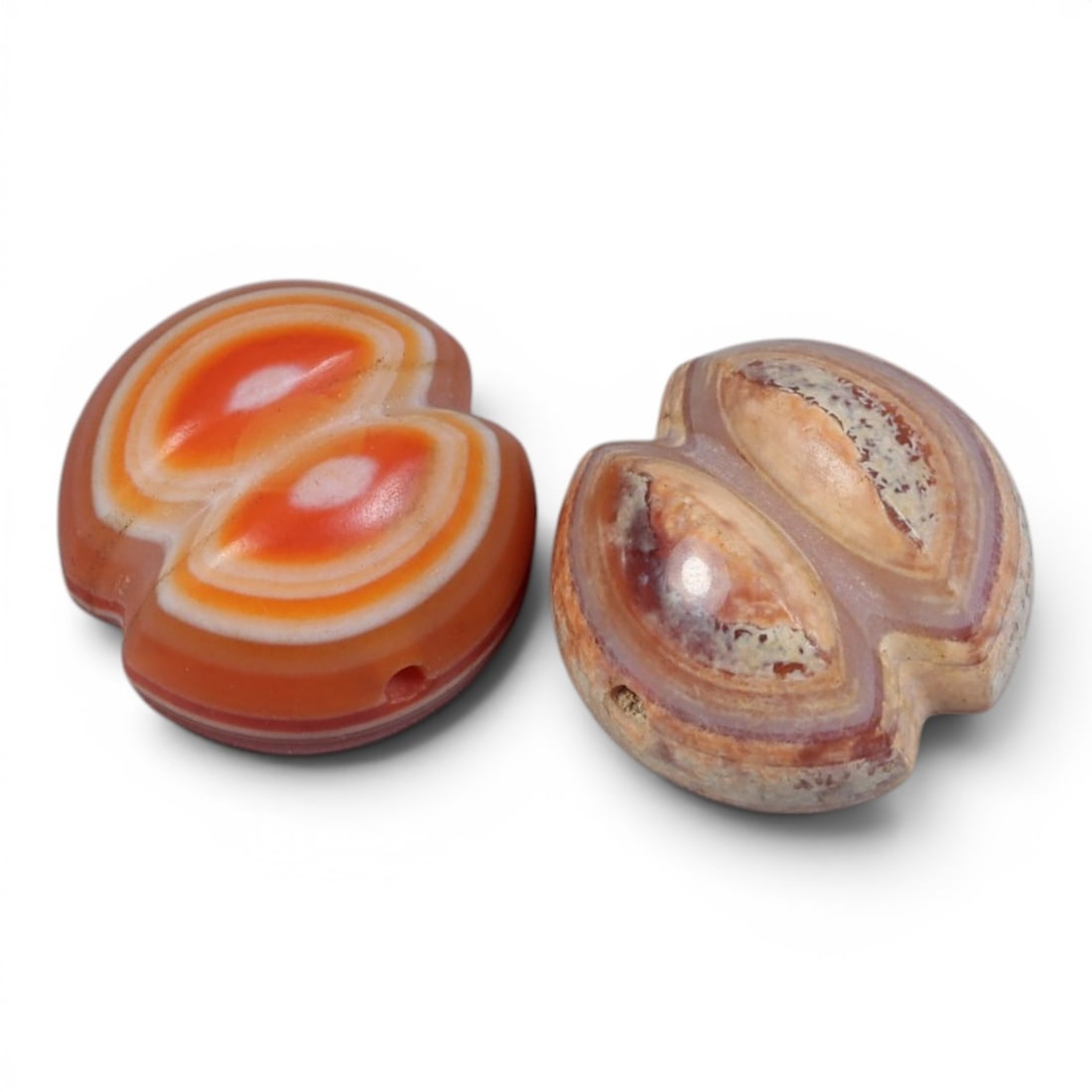 A Pair of Antique Himalayan Banded Carnelian Beads, 73AJ: The pair comprises two double-lobed carnelian beads, each displaying natural concentric banding. One bead features vibrant orange and white bands, while the other exhibits a more muted, patinated surf