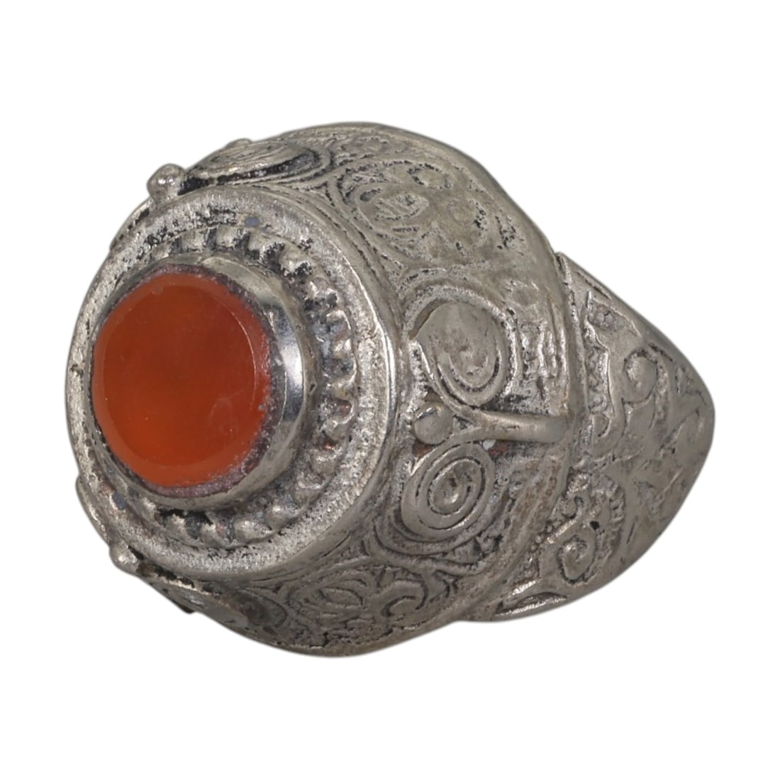 A Middle Eastern Silver Plated Carnelian Ring, Late 19th-Early 20th Century, 39AK: The ring is set with a round cabochon carnelian stone at the center of a domed bezel, framed by a raised, beaded border. The bezel and shoulders are decorated with incised scroll and spiral motifs, ch