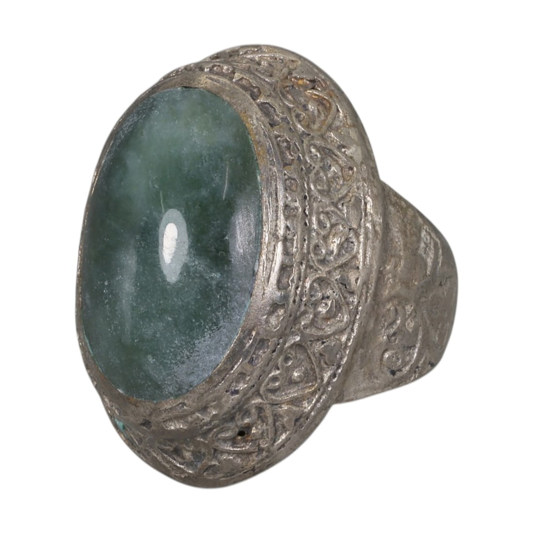 A Middle Eastern Silver Plated Green Agate Ring, Late 19th-Early 20th Century, 3AK: The ring is centered with a large oval cabochon green agate stone exhibiting natural mottled green tones, set within a domed bezel featuring intricate engraved foliate motifs. The shoulders are also d