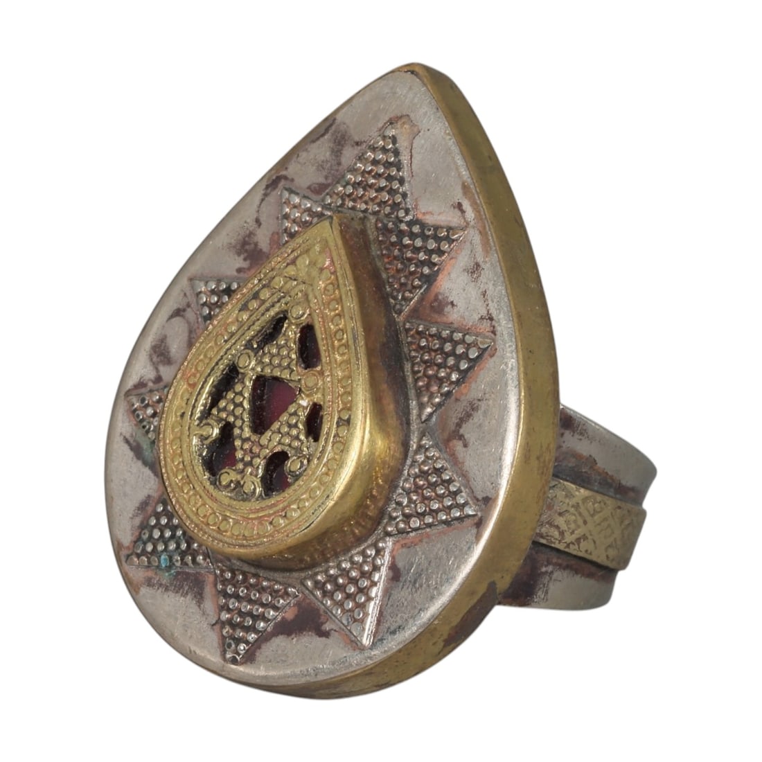 A Central Asian Silver Plated Teardrop Form Ring, Late 19th-Early 20th Century, 33AK: Crafted from silver plated metal with brass accents, featuring a wide, open band. The teardrop-shaped bezel displays a central raised teardrop panel with openwork detailing and a red inlay. The surrou