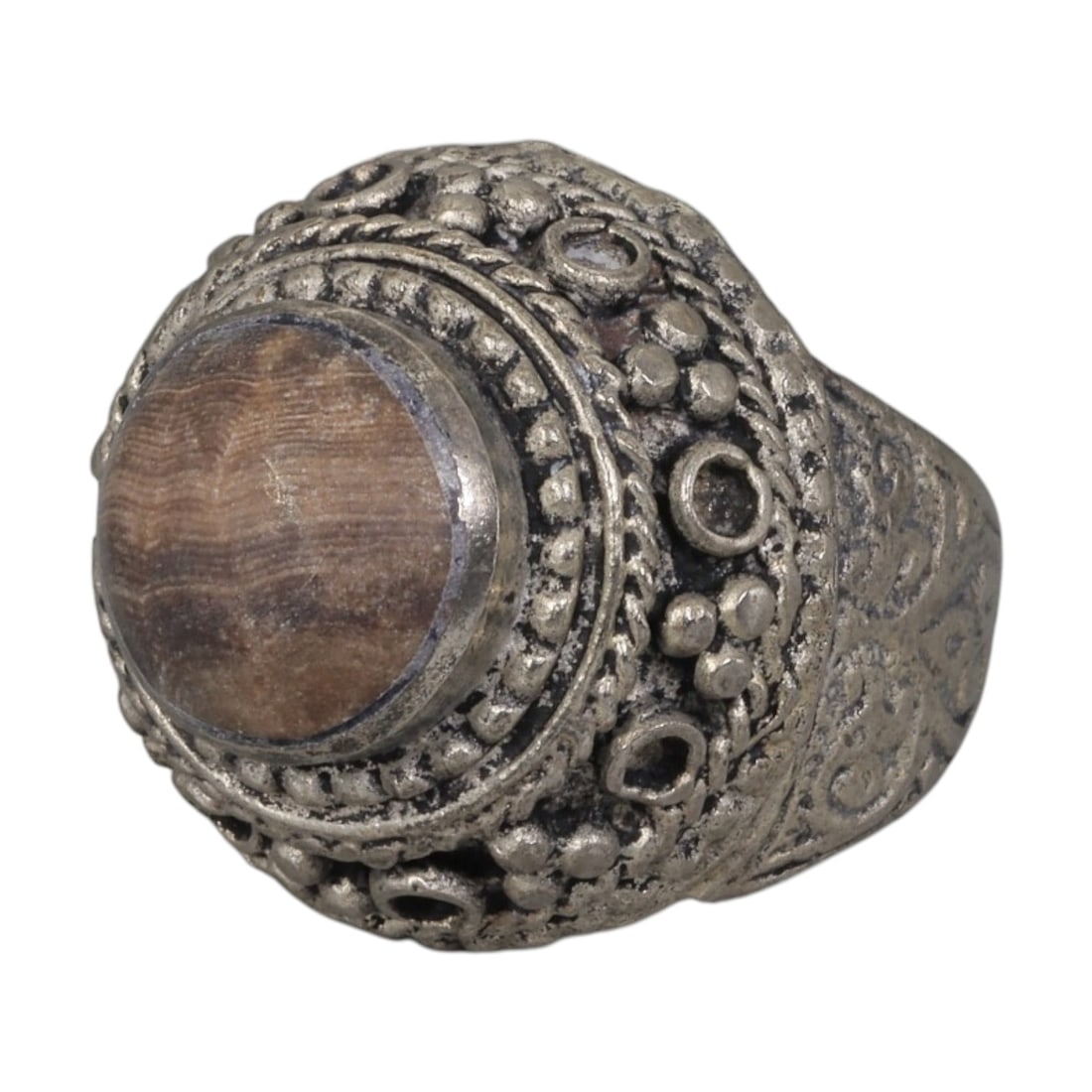 A Middle Eastern Silver Plated Banded Agate Ring, Late 19th-Early 20th Century, 6AK: The ring is centered with a round cabochon banded agate stone exhibiting natural layered brown striations, set within an ornate domed bezel decorated with beaded granulation, twisted wirework, and emp