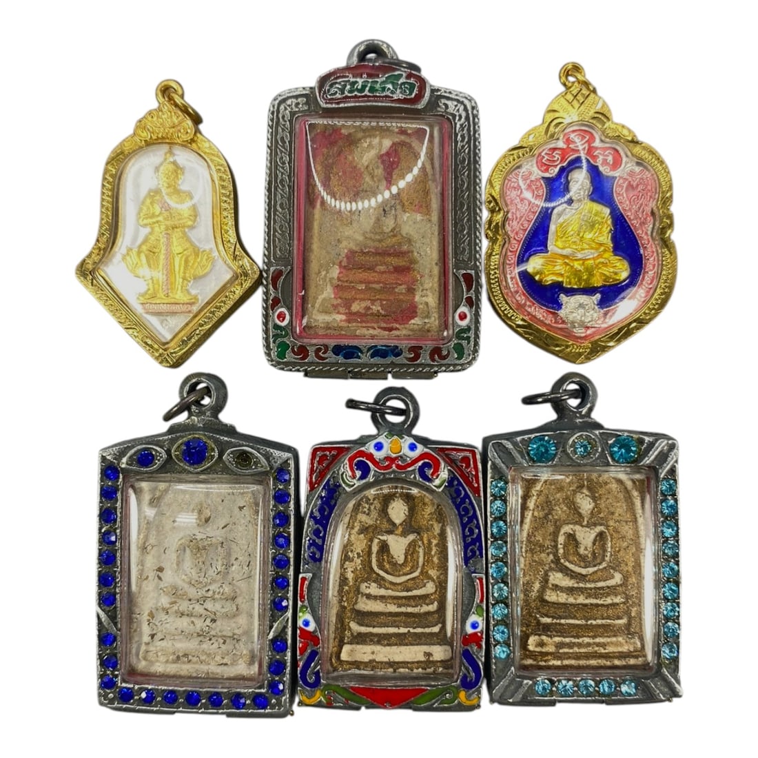 A Lot of 6 Vintage Thai Buddhist Amulets with Enamel and Jewel Accents, 8WS: This lot comprises six vintage Thai Buddhist amulets, each housed in ornate, decorated cases. The cases feature varied designs, including enamel detailing in red, blue, green, and pink hues, alongside