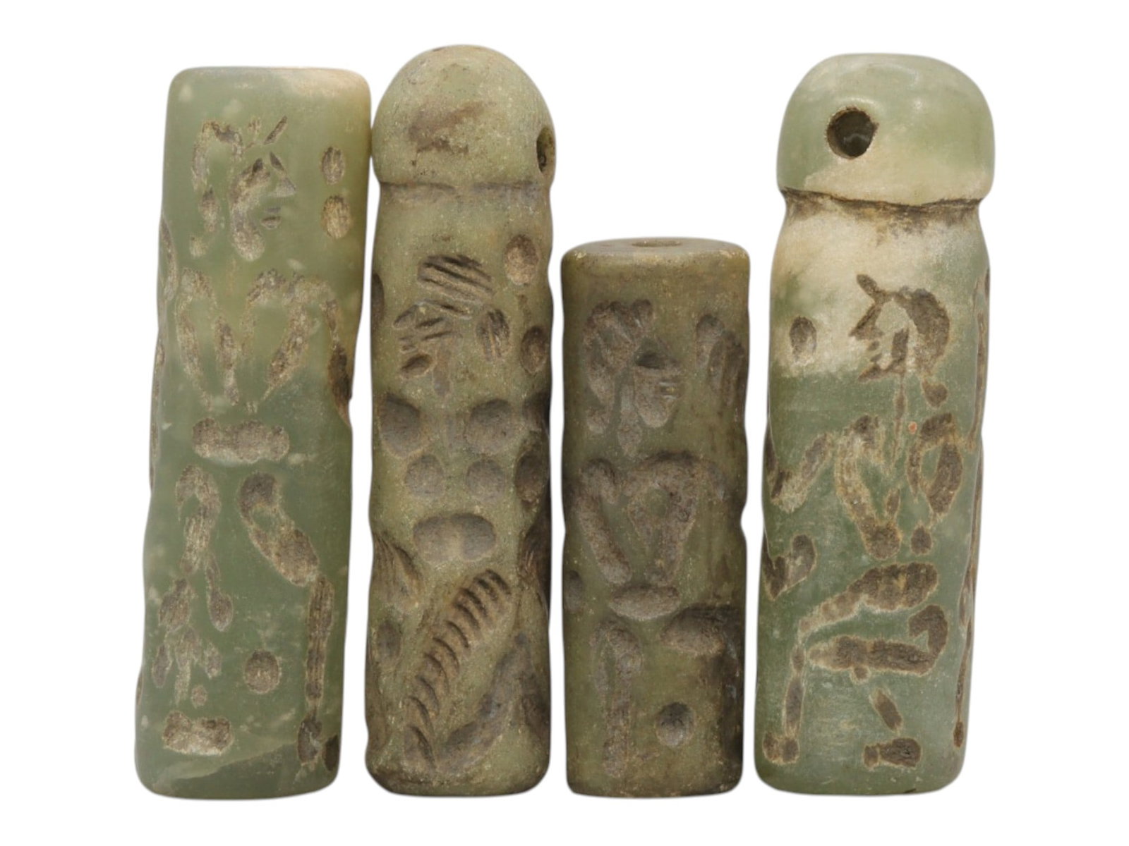 A Lot of 4 Ancient Mesopotamian Serpentine Cylinder Seals, 45WP: A curated lot of four ancient Mesopotamian-style cylinder seals, carved from serpentine stone with natural patination and wear consistent with age. Three seals feature domed tops with suspension holes