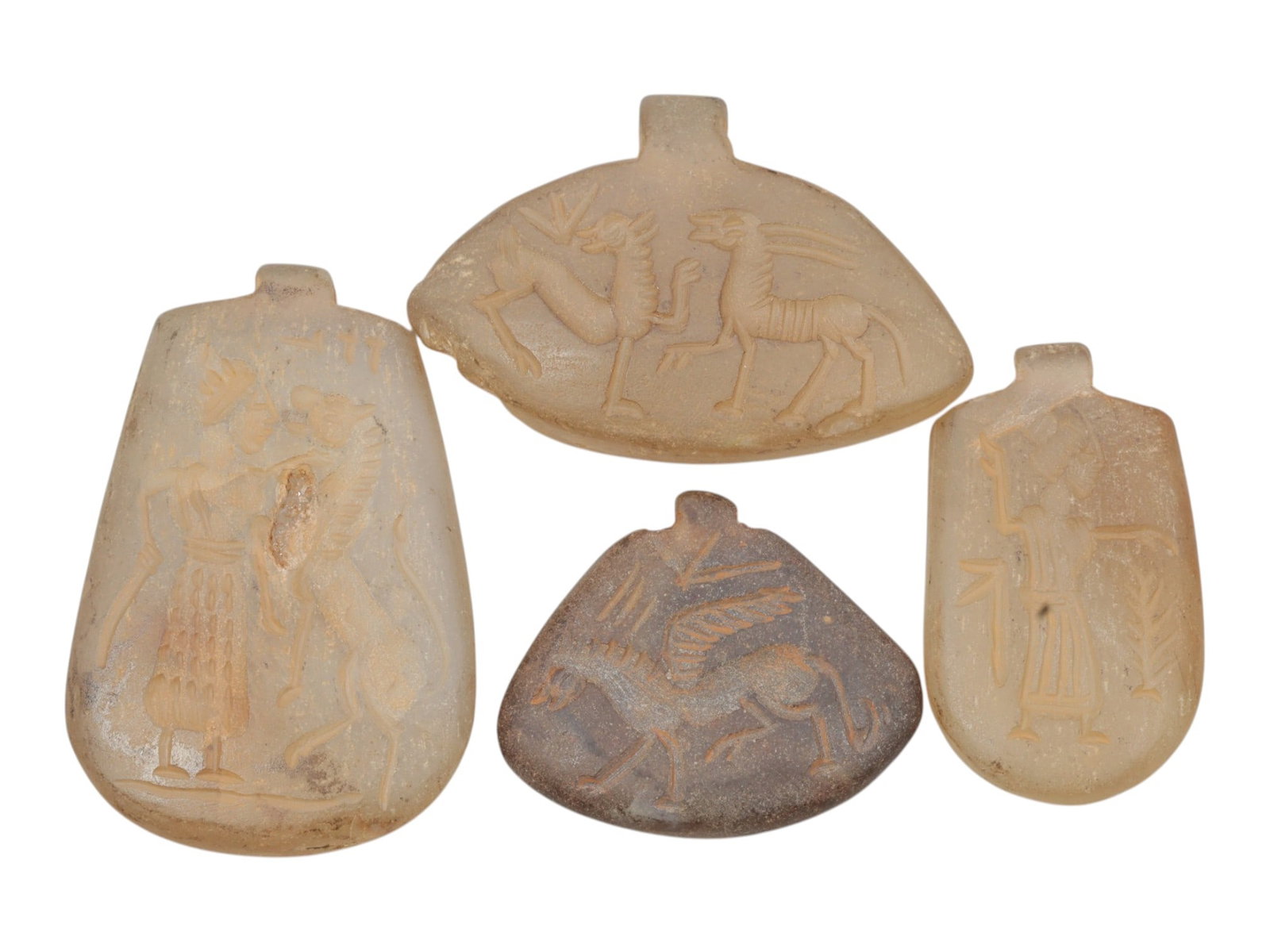 Lot of 4 Ancient Sasanian Chalcedony Amulet Pendants, Circa 3rd-7th Century CE, 62WT: Carved from chalcedony, the group consists of four distinct amulet pendants of varied forms. The set includes a large trapezoidal pendant depicting a standing figure interacting with a mythical beast,