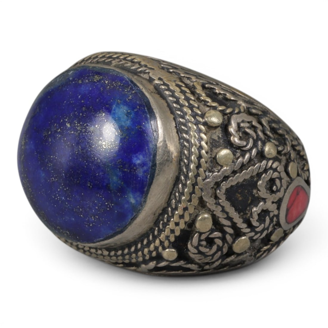 Antique Central Asian Silver and Lapis Lazuli Tribal Ring, 19th-Early 20th Century, 69AJ: The ring is set with a large, smooth cabochon lapis lazuli stone, displaying characteristic pyrite inclusions within its deep blue matrix. The silver mount is decorated with pseudo-filigree wirework, 