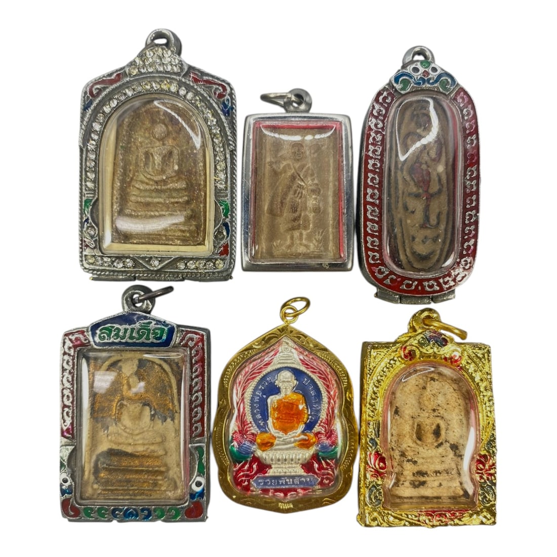 A Lot of 6 Vintage Thai Buddhist Amulets with Enamel and Jewel Accents, 7WS: This lot contains six vintage Thai Buddhist amulets, each set within ornate, decorated cases. The cases feature varied designs, including enamel detailing in red, blue, green, and pink hues, alongside