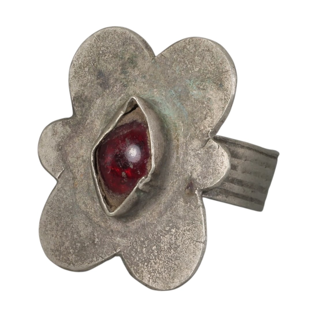 A Berber Silver Flower Form Ring, Late 19th-Early 20th Century, 19AK: Crafted from silver, featuring a wide band with parallel incised linear detailing. The flower-shaped bezel is centered with a red cabochon stone set in a simple folded metal bezel. The metal surface s